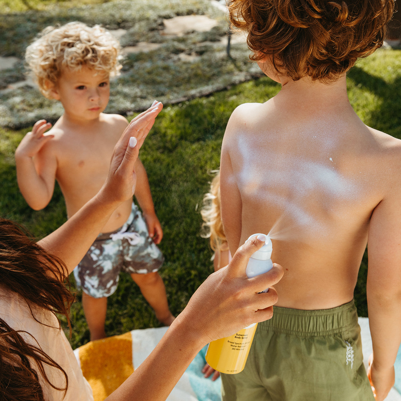 Mom is spraying Mineral Mist on her child's back outdoors.
